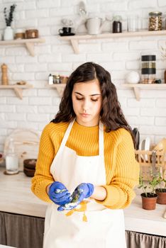 Beautiful brunette woman in yellow sweater and white apron coloring easter eggs in the kitchen