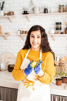 Beautiful brunette woman in yellow sweater and white apron coloring easter eggs in the kitchen