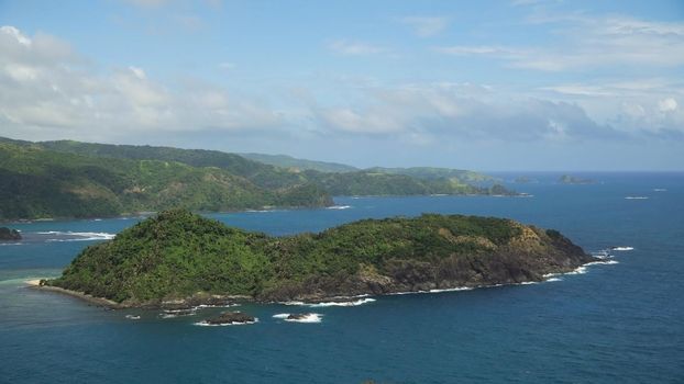 Topical island with the mountains and the rainforest on a background of ocean with big waves.Coast, sea and the tropical island with rocks, beach and waves. Seascape: sky, clouds, ocean. Philippines, Catanduanes. Travel concept.