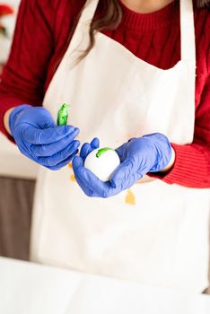 Beautiful brunette woman in red sweater and white apron coloring easter eggs in the kitchen opening tube with color liquid