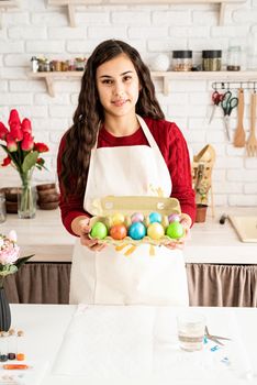 Beautiful smiling brunette woman in red sweater and white apron holding colorful easter eggs