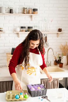 Beautiful smiling brunette woman in red sweater and white apron decorating colorful easter eggs