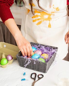 Beautiful smiling brunette woman in red sweater and white apron decorating colorful easter eggs