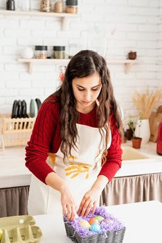 Beautiful smiling brunette woman in red sweater and white apron decorating colorful easter eggs