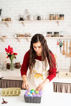 Beautiful smiling brunette woman in red sweater and white apron decorating colorful easter eggs