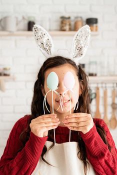 Beautiful funny brunette woman in red sweater and white apron covering eyes with easter eggs decorations