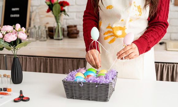 Beautiful smiling brunette woman in red sweater and white apron decorating colorful easter eggs
