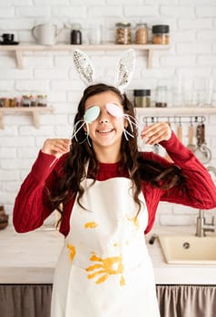 Beautiful funny brunette woman in red sweater and white apron wearing rabbit ears, covering eyes with easter eggs decorations