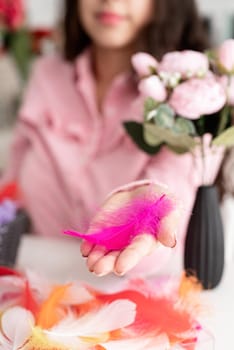 Beautiful smiling brunette woman in pink dress decorating colorful easter eggs with colorful feathers