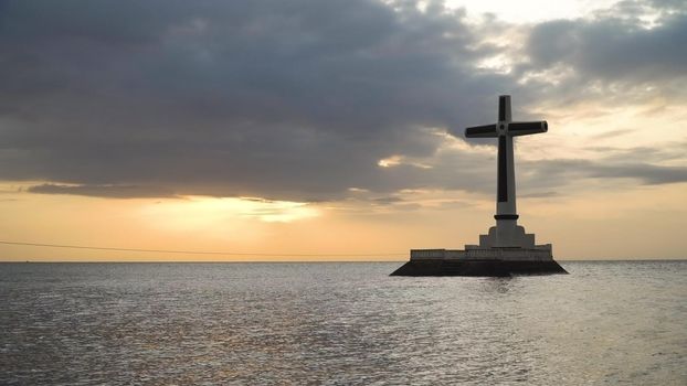 Sunken Cemetery cross in Camiguin Island, Philippines. Large crucafix marking the underwater sunken cemetary of the coast of camiguin island near mindanao in the Philippines. Catholic cross in the water on the background of sky and clouds.. The Sunken Cemetery marks the swept remains of locals when Mt. Vulcan Daan. Travel concept.