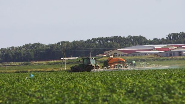 Aerial view tractor spraying the chemicals on the large green field. Spraying the herbicides on the farm land. Treatment of crops against weeds.