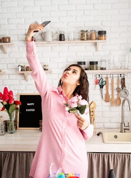 Beautiful brunette woman taking selfie using mobile phone in the kitchen