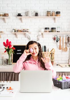 Funny woman greeting her friends online, celebrating easter, covering her eyes with colorful eggs