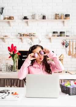 Funny woman greeting her friends online, celebrating easter, covering her eyes with colorful eggs