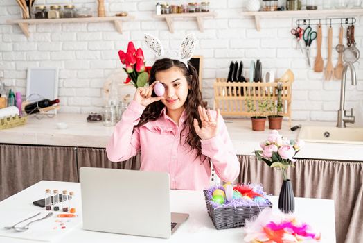 Funny woman greeting her friends online, celebrating easter, covering her eyes with colorful eggs