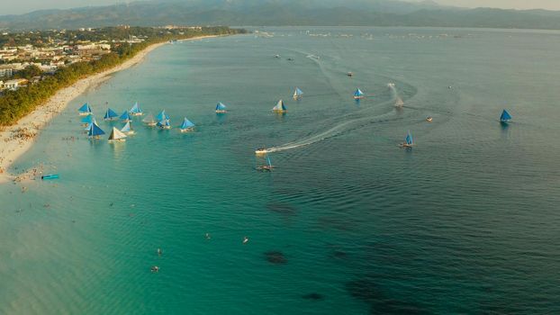 Aerial view of sailing yachts on the sandy beach of Boracay Island at sunset time. Tropical white beach with sailing boat. Summer and travel vacation concept.