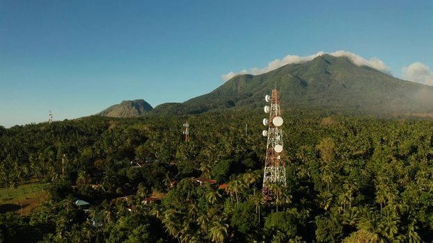 Antennas and microwaves link dishes of mobile phone network and TV transmitter on telecommunication towers with mountains and rainforest. Camiguin, Philippines