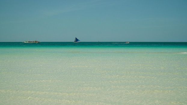 Sailing boat in crystal clear turquoise water, from above. Sailing yacht glides over the waves, Boracay, Philippines.