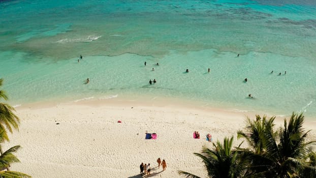 aerial view beach with tourists on tropical island, palm trees and clear blue water. Malcapuya, Philippines, Palawan. Tropical landscape with blue lagoon