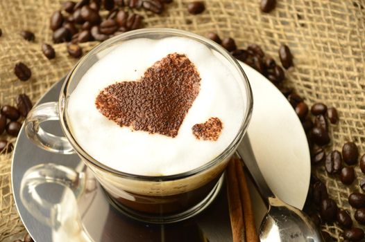 A specialty cup of brewed coffee with a heart shape design while resting among roasted beans.