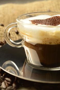 A specialty cup of brewed coffee with a heart shape design while resting among roasted beans.