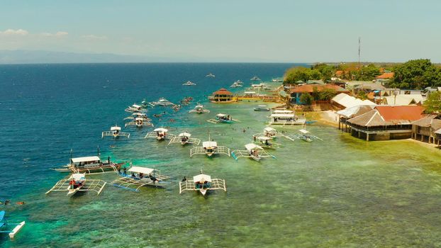 Tourists snorkeling over coral reef with clear blue ocean water, aerial view. Moalboal, Philippines. People swim in the transparent sea between coral reefs. Summer and travel vacation concept.