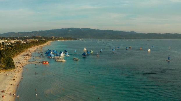 White beach on Boracay island with tourists and sailing boats at sunset time, top view. Tropical white beach with sailing boat. Summer and travel vacation concept.