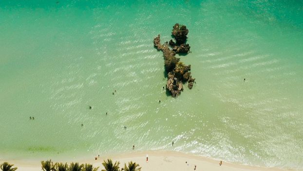 White Beach of Boracay and people swim at turquoise azure sea near Grotto Willy's Rock upon which stands the Virgin Mary Statue. Copy space for text. Summer and travel vacation concept.