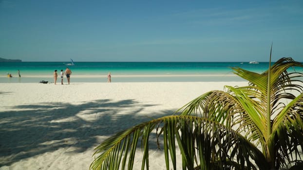 Tourists on a sandy beach and blue sea through palm branches. Summer and travel vacation concept. Boracay, Philippines