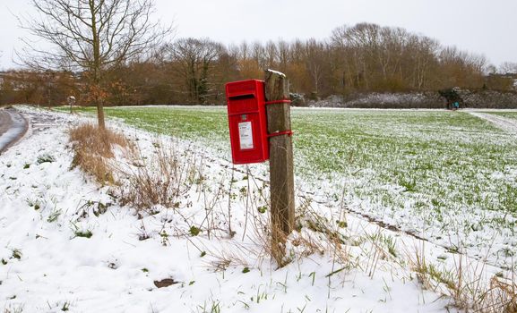 Red British post box, winter time. Pole mounted English mailbox in the countryside. Winter, snowy day