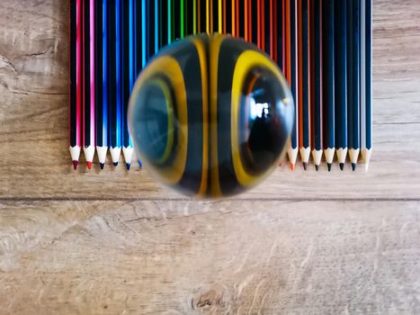 Colorful pencil crayons lie in on wooden floor with crystal glassy lensball on it