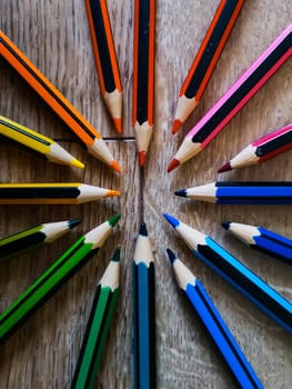 Colorful pencil crayons lie in a circle on wooden floor