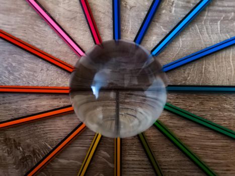 Colorful pencil crayons lie in a circle on wooden floor with crystal glassy lensball