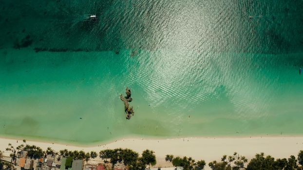 White Beach of Boracay and people swim at turquoise azure sea near Grotto Willy's Rock upon which stands the Virgin Mary Statue. Copy space for text. Summer and travel vacation concept.