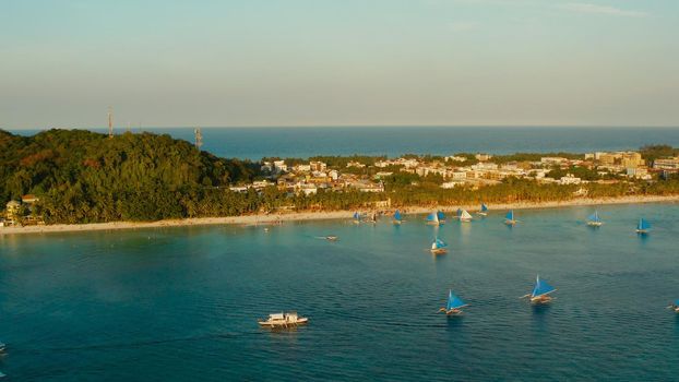 Aerial view of sailing yachts on the sandy beach of Boracay Island at sunset time. Tropical white beach with sailing boat. Summer and travel vacation concept.