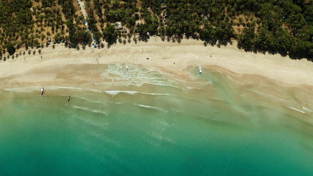 Tropical sandy beach with tourists in blue water, aerial view. Nagtabon. Palawan, Philippines. Seascape with lagoon in sea, sand, palm trees. Summer and travel vacation concept