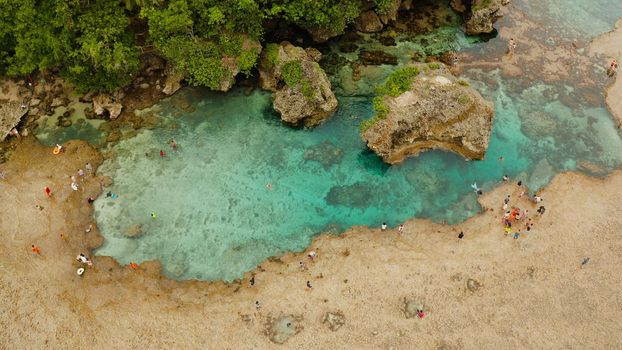 Natural pools on the rocky shore with tourists formed at low tide. Magpupungko natural rock pools. Siargao, Philippines.