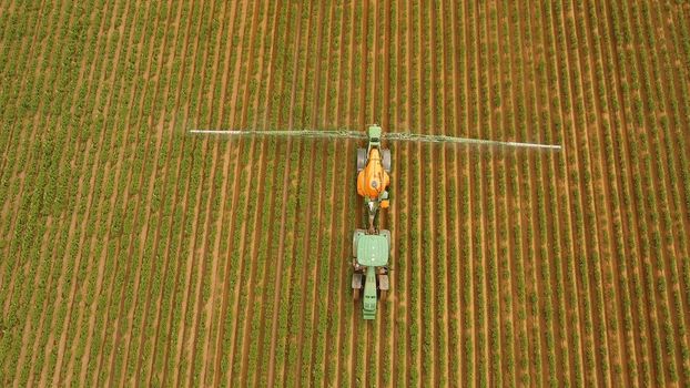 Aerial view tractor spraying the chemicals on the large green field. Spraying the herbicides on the farm land. Treatment of crops against weeds.