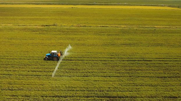 Aerial view tractor spraying the chemicals on the large green field. Spraying the herbicides on the farm land. Treatment of crops against weeds.