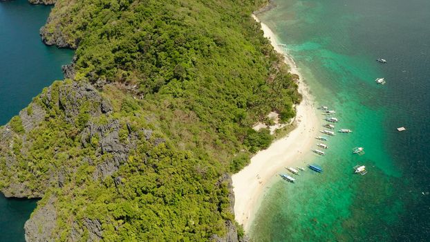 aerial view tropical beach on island with palm trees, blue lagoon and azure clear water. tourist boats on coast tropical island. Helicopter Island in El Nido, Palawan Philippines. Tropical landscape with blue lagoon, coral reef