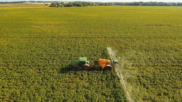 Aerial view tractor spraying the chemicals on the large green field. Spraying the herbicides on the farm land. Treatment of crops against weeds.