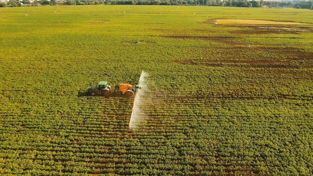 Aerial view tractor spraying chemicals on large green field. Spraying the herbicides on the farm land. Treatment of crops against weeds.