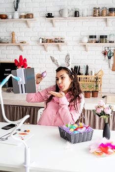 Funny woman greeting her friends online, celebrating easter, covering her eyes with colorful eggs