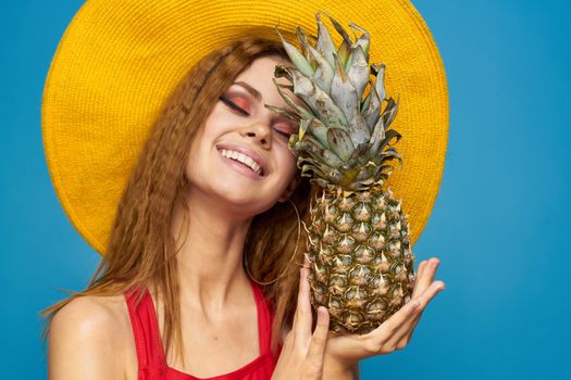 Woman in yellow hat with pineapple in hands emotions fun lifestyle summer fruit blue background. High quality photo