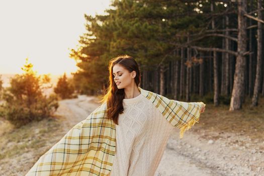 Traveler with a blanket on her shoulders near the trees on the road in the park. High quality photo