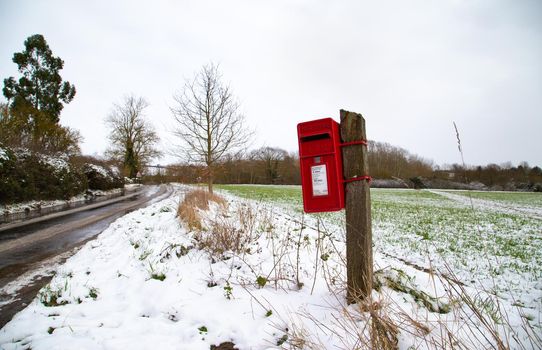 Red British post box, winter time. Pole mounted English mailbox in the countryside. Winter, snowy day