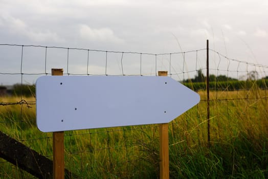 white wooden empty signpost placed in front of a grass field with a fence
