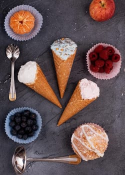 three ice cream, raspberry, blueberry, muffin, apple, and tangerine on grey background. View from above.