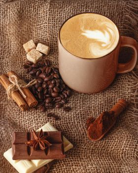 cup of coffee with cinnamon, anise, coffee bean, chocolates and sugar on a wooden background