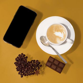cup of coffee with chocolate, heart shape beans, phone on a table